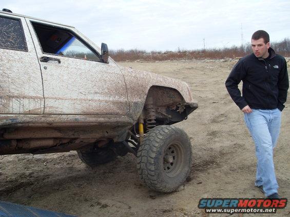 Mud-covered 1984 Jeep Cherokee XJ parked on dirt with a man standing nearby