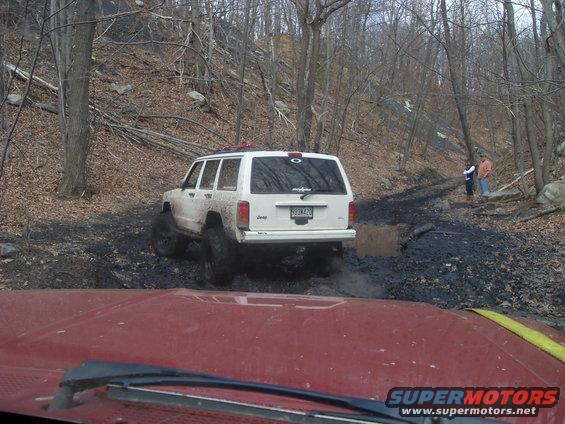 White Jeep Cherokee with mud on tires, seen from behind on a dirt road