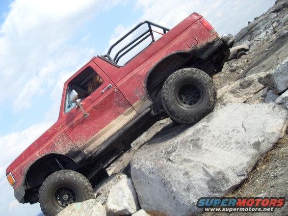 Red 1987 Ford Bronco climbing over large rocks on a trail