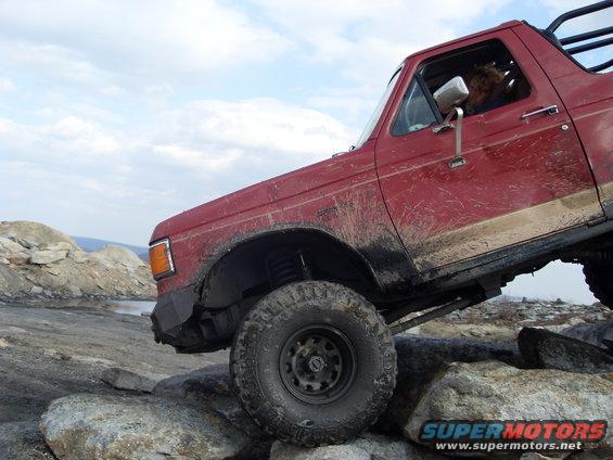 Red 1987 Ford Bronco climbing rocks, 3/4 front view