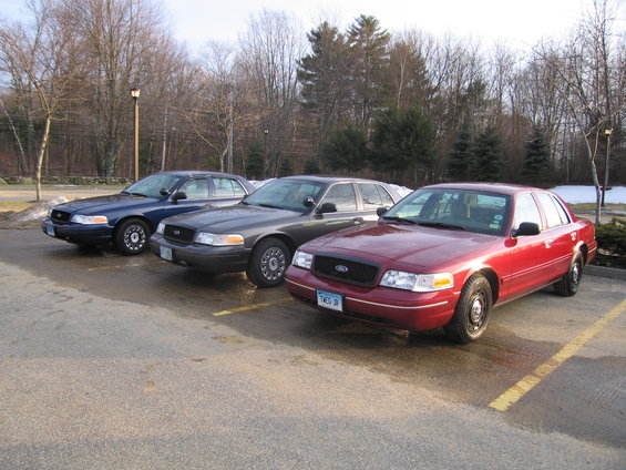 Red 2001 Ford Crown Victoria front 3/4 view with two other Crown Victorias behind it