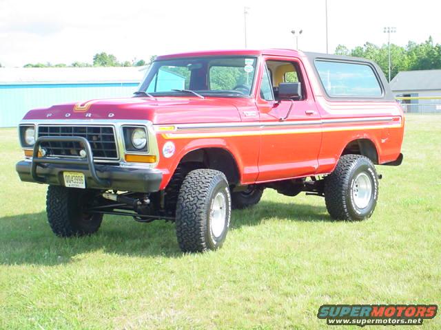 Red 1978 Ford Bronco with orange stripe, parked on grass, 3/4 front view