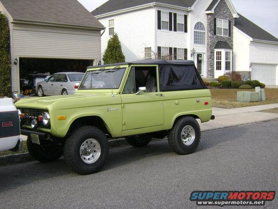 Lime green 1974 Ford Bronco with a black soft top, parked on a residential street