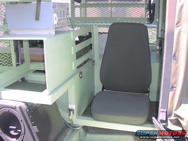 Interior of a military vehicle showing a seat, equipment rack, and speaker