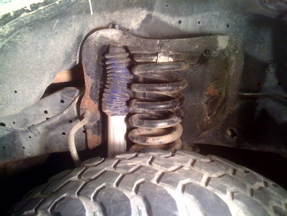 Close-up of a vehicle's front tire, coil spring, and shock absorber assembly