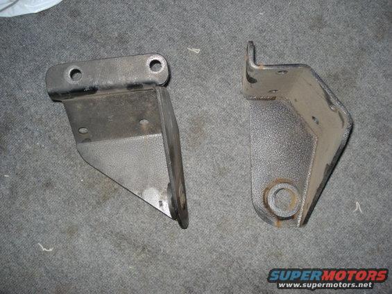 Two metal brackets on a carpeted surface. One bracket has two holes on top and a triangular plate. The other bracket is L-shaped with a circular hole at the bottom