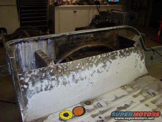 Vehicle body section with visible welding and body filler, showing interior wheel well. Two sanding discs are on the floor