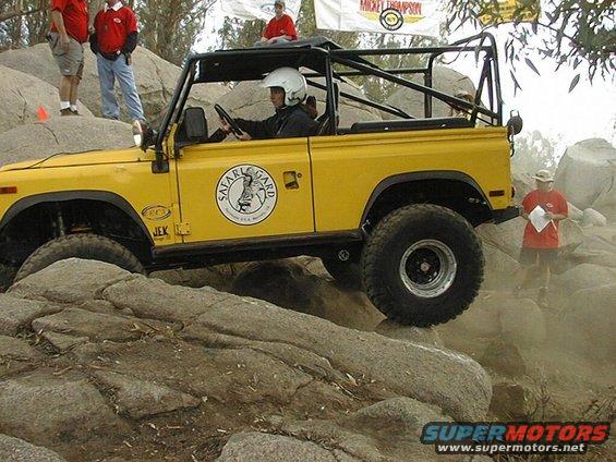 Yellow off-road vehicle with a roll cage climbing over rocks. Driver wears a helmet. "Safari Guard" logo on door