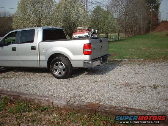 Silver pickup truck parked on gravel, carrying a V8 engine in its bed