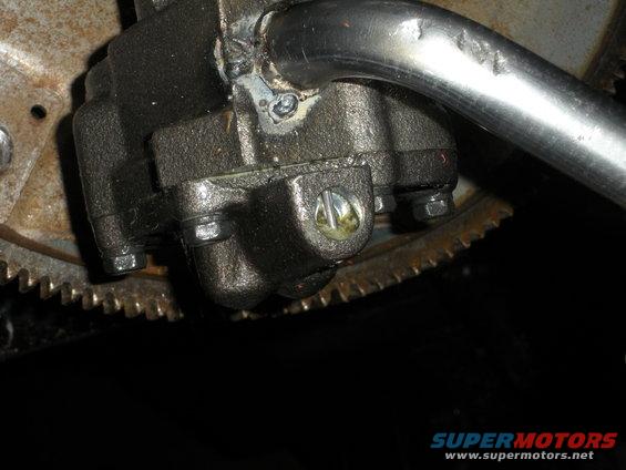 Close-up of an engine oil pump assembly with a metal tube and a toothed flywheel