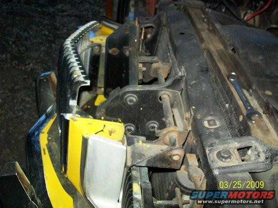 Yellow and black painted hood latch mechanism with metal bracing and a wrench nearby