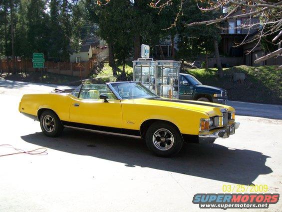 Yellow 1973 Mercury Cougar convertible parked on pavement, black stripe on hood and side