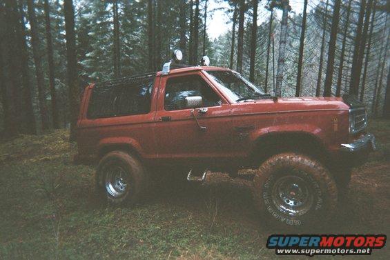 1988 Ford Bronco II parked in a wooded area, with aftermarket lights on the roof