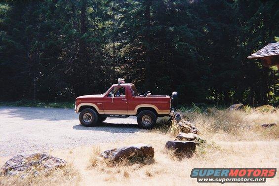 1985 Ford Bronco parked on gravel with trees and rocks