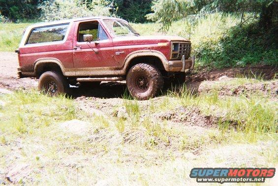 Red Ford Bronco with a white top driving off-road