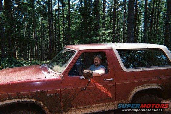 Red 1985 Ford Bronco in forest, driver visible