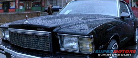 Black coupe with chrome grille and hood ornament, wet from rain. Visible text 'SuperMotors'