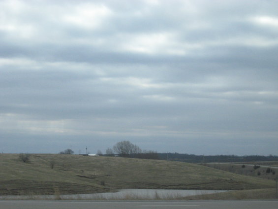 Overcast sky above rolling hills and a small pond