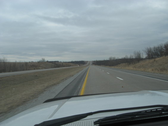 View of a highway stretching into the distance under a cloudy sky, seen from the perspective of a car's dashboard