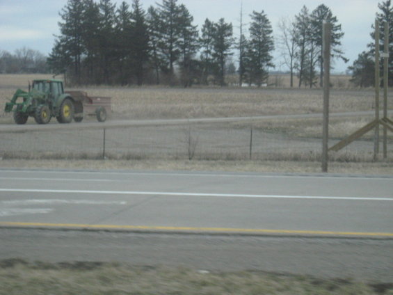 Green tractor pulling a red trailer on a dirt road next to a highway