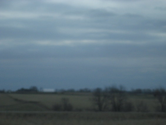 Overcast sky above a blurry rural landscape with trees and fields