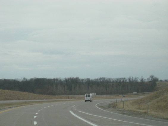 White van driving on a highway with trees in the background
