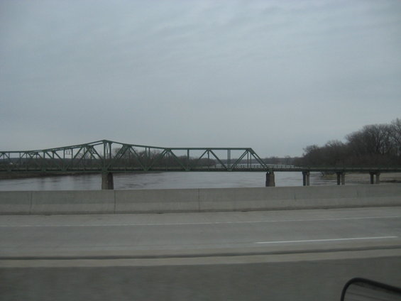 Green truss bridge over a wide river under a cloudy sky