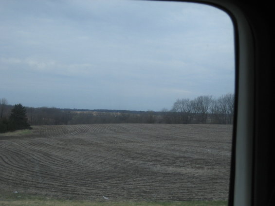view of plowed field and bare trees from inside a vehicle