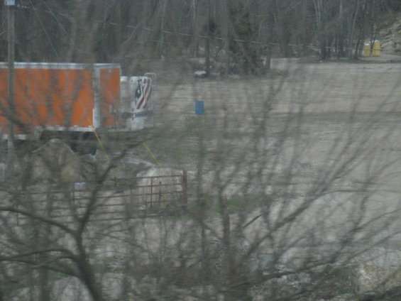 Orange trailer parked at a construction site with a blue barrel and a fence