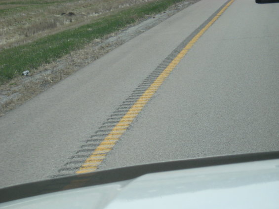 View from inside a vehicle looking at a highway lane with a yellow dashed line and rumble strip