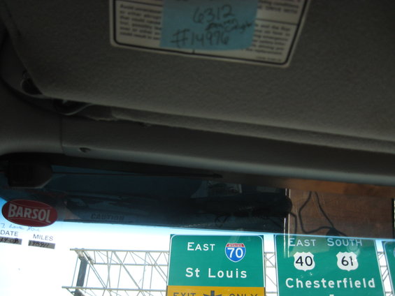 Inside vehicle, sun visor has a blue sticky note with numbers. Road signs for East 70 St Louis and East South 40 61 Chesterfield visible through windshield