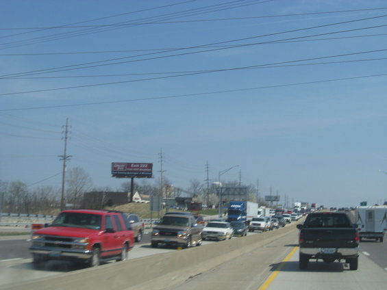 Highway traffic jam with multiple cars, trucks, and a trailer under a blue sky