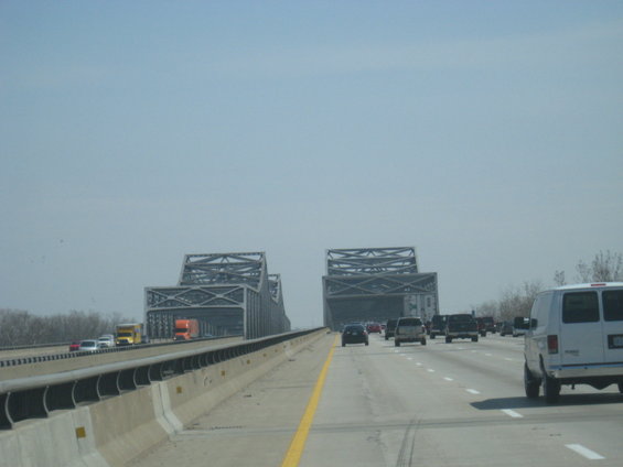 White van driving on a highway with a large bridge in the background