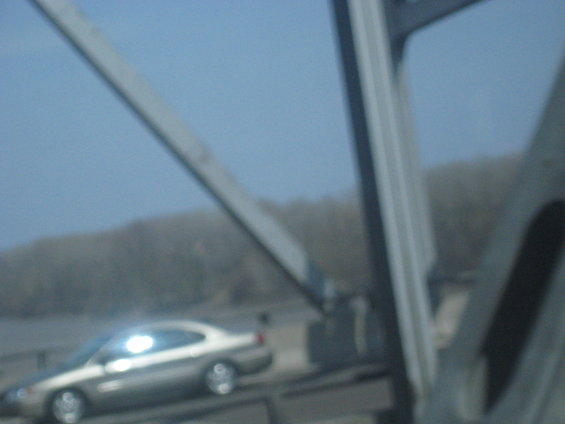 Silver coupe driving on a bridge with a clear blue sky