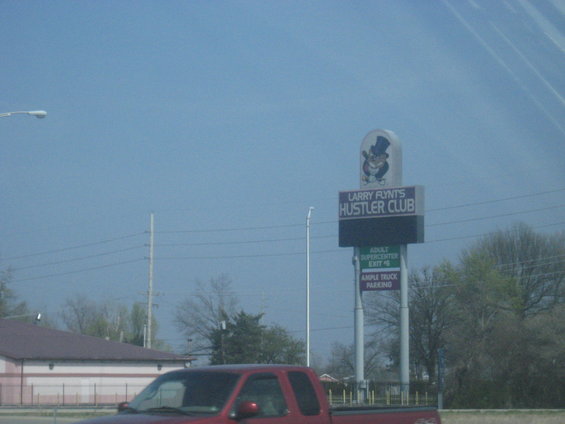 Roadside sign for Larry Flynt's Hustler Club with exit information and ample truck parking