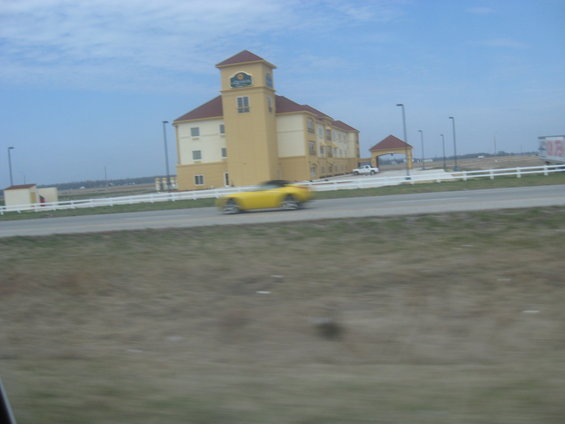 Yellow convertible in motion on a road with a hotel in the background