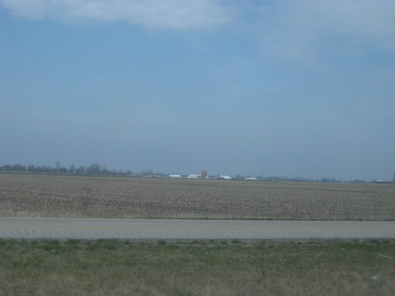 Farm buildings and harvested fields under a hazy blue sky