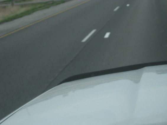 White vehicle hood seen from inside, driving on a highway with lane markings