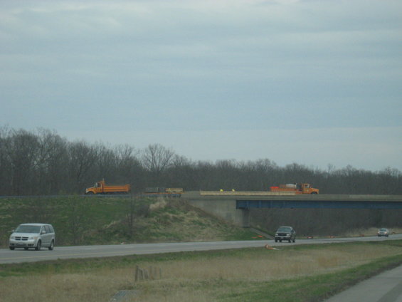 Construction trucks driving on an overpass above a highway with other vehicles