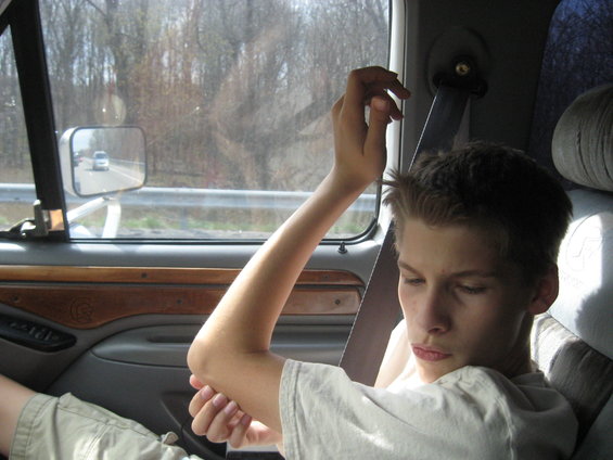 Interior view of a vehicle with a young person in the passenger seat, another car visible in the side mirror