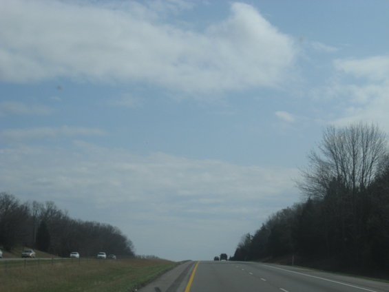 Driving on a highway with trees and clouds