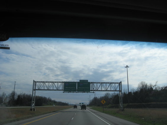 Highway overhead signs indicating directions to Memphis and Nashville, with two vehicles on the road