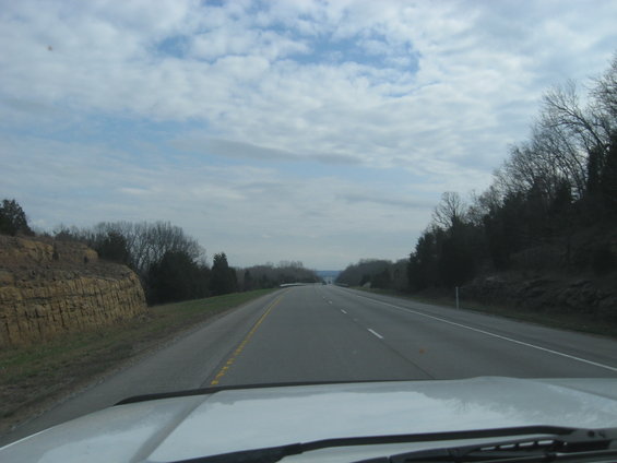 Dashboard view from a vehicle driving on a highway with trees and a rock formation on the side