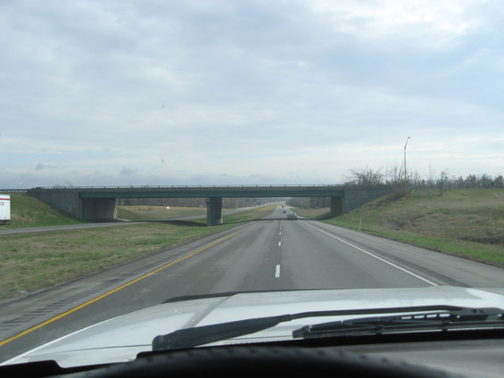View from inside a vehicle looking down a highway towards an overpass with a cloudy sky