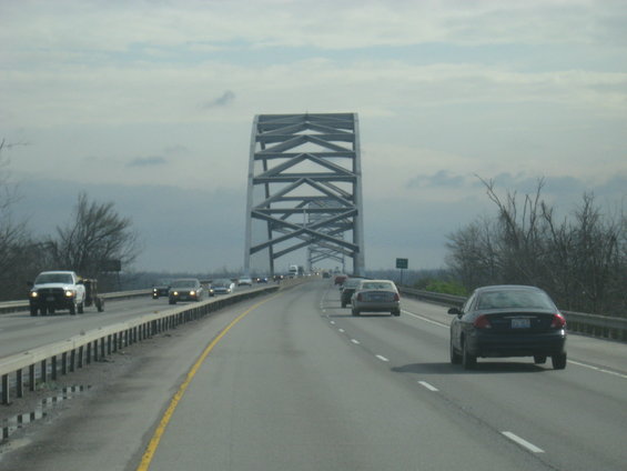 Cars driving on a highway bridge with a large metal truss structure