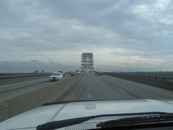 Driving on a highway overpass with a large metal bridge structure in the distance and other cars on the road