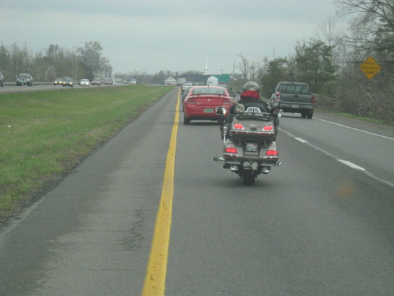 Motorcycle riding on highway behind a red car and in front of a pickup truck