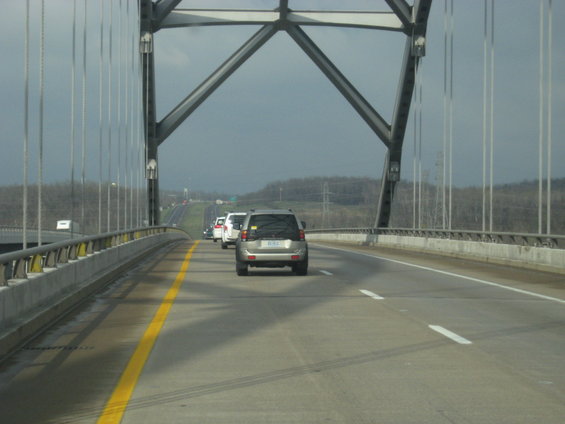 Silver SUV on a bridge with other cars, under a cloudy sky