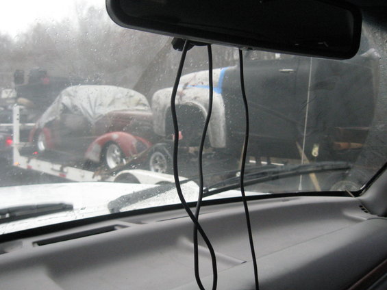Two cars on a trailer, one red and covered, one white and partially covered. View from inside a vehicle
