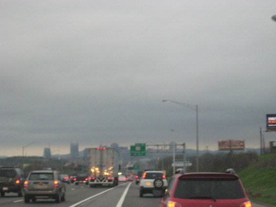 Highway traffic with city skyline in distance under cloudy sky